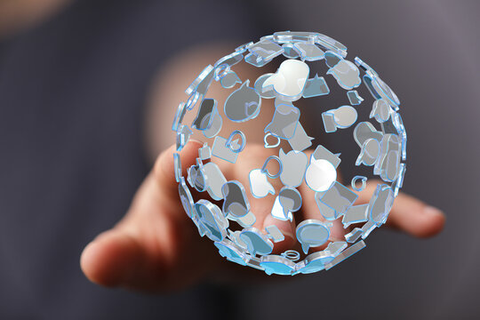 Close-up of a hand holding a transparent globe with speech bubble and message icons, illustrating communication, connection, and social media. I