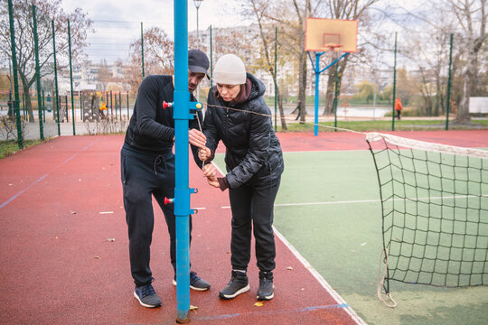 A man and woman collaboratively set up a net on an outdoor multisport court, preparing for an active game in a park setting. Perfect for themes of teamwork, outdoor sports, and recreation.
