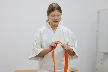 A girl puts on a kimono and ties a belt in the gym locker room.