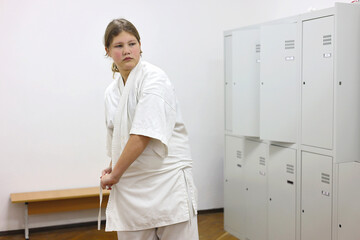 A girl puts on a kimono and ties a belt in the gym locker room.