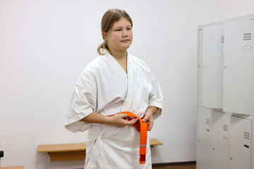 A girl puts on a kimono and ties a belt in the gym locker room.