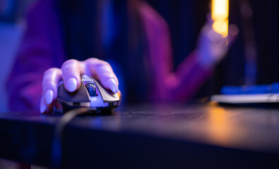 Close-up of a hand holding a gaming mouse during active computer use in a neon-lit environment