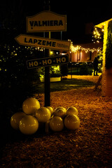 Valmiera,Latvia-November 30,2025-Festive outdoor Christmas scene with decorative signposts, glowing lights, evergreen trees and white ornaments on a warmly lit pathway.