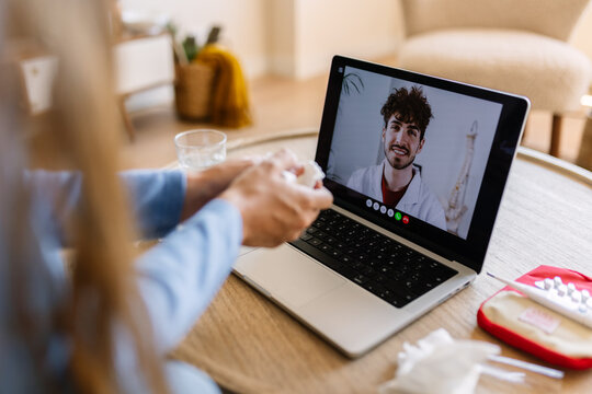 Female patient holding tissue while consulting male doctor online. Sick young woman talking with smiling physician on laptop. Health and remote care concept.