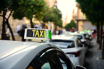 A row of city taxis captured with shallow depth of field. A sharp TAXI sign in the foreground...
