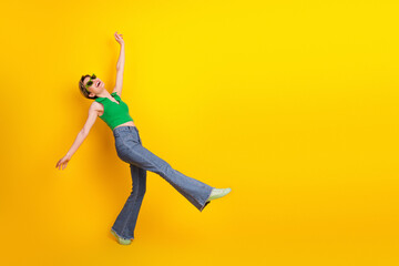 Obraz premium Young woman in green top and jeans jumping against a yellow background for lifestyle fashion image