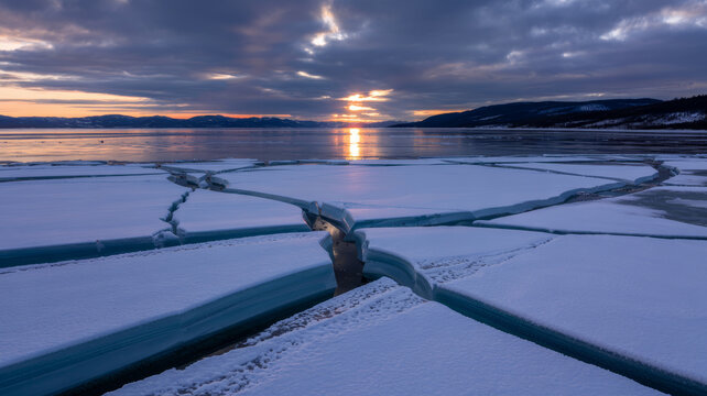 Cracked ice and serene water under a dramatic sunrise sky.