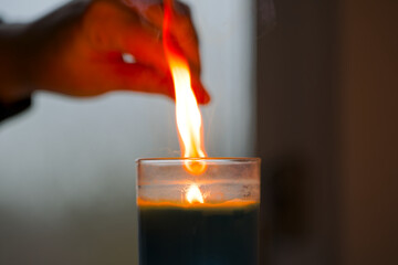 Close-up of female hand with burning match and candle in a glass and window in the background. Photo taken December 3rd, 2025, Zurich, Switzerland.