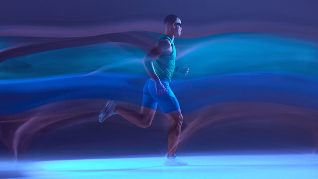 Runner in neon studio colors sprinting across glowing motion trails. Concept of athletic performance visuals, cardio training content, running gear promotion, and speed-focused fitness campaigns.