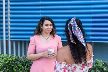 Women friends having casual conversation outdoors with travel mug