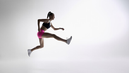 Dynamic female runner jumping forward in mid-air on clean studio background. Concept of sports...