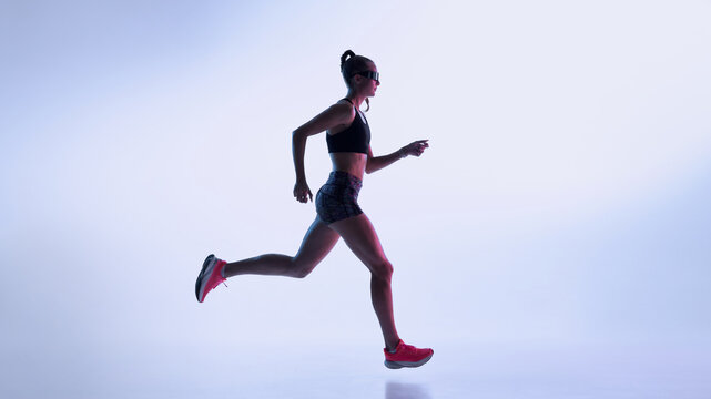 Female athlete running in neon gradient studio with modern sport aesthetics. Concept of fitness marketing, cardio training visuals, performance coaching, and dynamic sportswear promotion.
