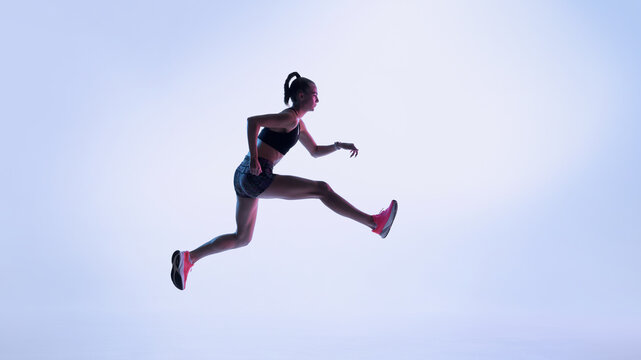 Futuristic female athlete performing dynamic leap in neon light. Concept of performance training, speed progression, modern sports visuals, and energetic fitness storytelling. - Powered by Adobe
