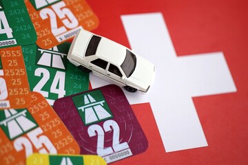 Switzerland vignette stickers for different years with toy car on Swiss flag close up. Driving permit and registration concept