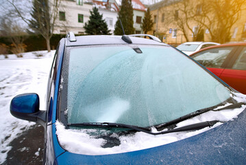 Frozen car windshield covered in white frost, parked car with its windshield completely frosted,...