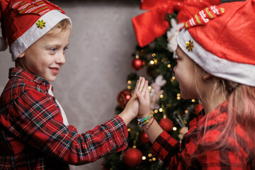 A boy and a girl in matching Christmas pajamas giving each other a high-five after decorating the...