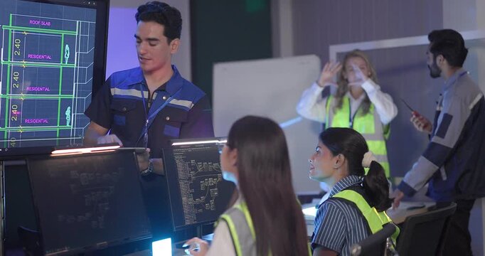 Engineers in high visibility vests collaborate in control room, reviewing digital site plans and dashboards during an operations and safety discussion. Coordination, monitoring, and incident readiness