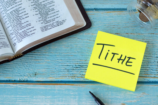 Tithe, handwritten text on note with holy bible and coin money on wooden table. Top view. Christian biblical concept of giving, offering, and blessing from God Jesus Christ.