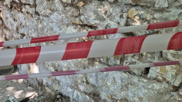 Warning tape, safety, construction site barrier of red and white striped plastic tape against a rough stone wall, indicating restricted access.