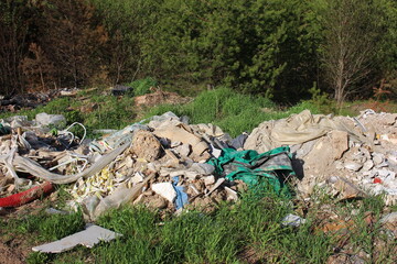 Mound of construction debris and plastic sheeting illegally dumped in a grassy, wooded area during late spring