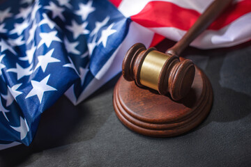 A judge gavel on sound block with American flag on a black surface, symbolizing justice and patriotism.