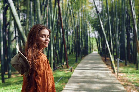 Woman bamboo path hat portrait nature forest walkway - young woman with straw hat over shoulder standing on a bamboo forest path, peaceful portrait and travel mood in lush green nature.