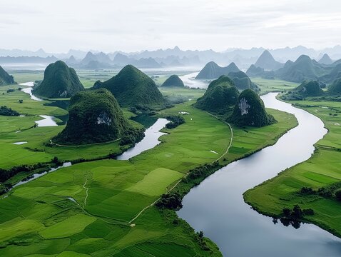 An aerial view of a lush green landscape featuring a winding river, rolling hills, and distant mountains under a misty sky. The scene is dominated by vibrant gr