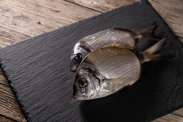 Raw two-banded seabream on granite plate over rustic wooden background. Fresh two-banded seabream displayed on granite serving board. Freshly caught two-banded seabream on granite tray.