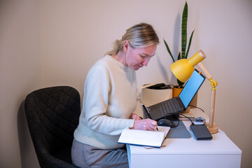 Woman writing in notebook while working at home office desk