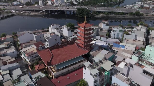 Orbit CCW drone view over Buddhist pagoda in busy urban area of Ho Chi Minh City, Vietnam on a sunny clear day featuring transportation infrastructure of main roads and canals in background