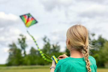 Back view female kid girl flies colorful kite open field, focusing movement wind while enjoying...