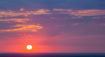 A breathtaking sunset with the sun low on the horizon, casting vibrant hues of pink, orange and purple across the sky. Soft clouds reflect the warm glow, creating a serene, dreamy atmosphere
