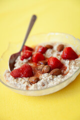 A bowl of creamy oatmeal topped with fresh strawberries and almonds, drizzled with honey. Served on a vibrant yellow background with a spoon ready for a healthy, delicious breakfast