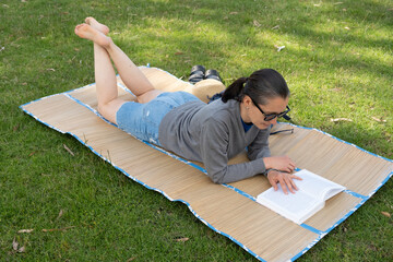 Woman relaxing and reading on grass mat in park.