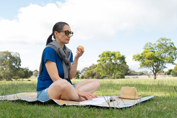 Woman enjoying picnic in sunny park, reading book and eating pear.