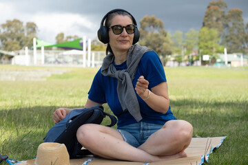 Caucasian female adult relaxing with headphones in park on cloudy day.