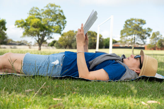 Caucasian adult female relaxing outdoors reading in park.