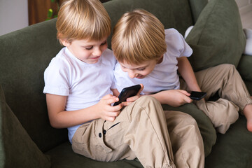 kids blonde boys twins using smartphones on the couch in living room