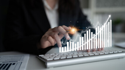 A business professional engages with a computer keyboard while a digital graph showcases financial growth, highlighting modern technology in a corporate setting. Impute