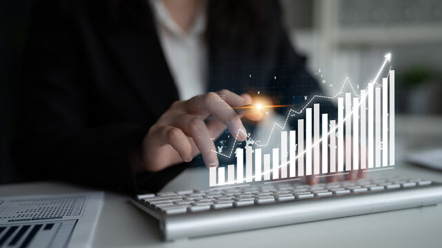 A business professional engages with a computer keyboard while a digital graph showcases financial growth, highlighting modern technology in a corporate setting. Impute - Powered by Adobe