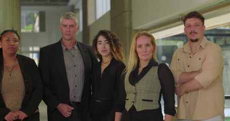 Smiling business team posing closely in bright office hallway, diverse group of professionals standing together for casual workplace portrait with positive expression