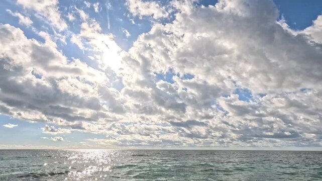 Ocean clouds sky, bright sun shines through scattered clouds over sparkling ocean water, scenic nature weather view