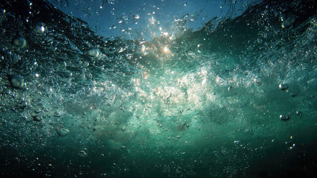 An immersive underwater view captures brilliant sunlight piercing a turbulent ocean surface, filled with countless swirling air bubbles creating a dynamic aquatic spectacle below.