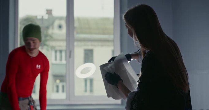 Silhouette of a female tattoo artist preparing a client for a session, standing against a window and a ring light in a studio