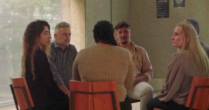 Support group sitting in circle, quietly listening to woman share vulnerable story during intense moment of emotional connection and empathy