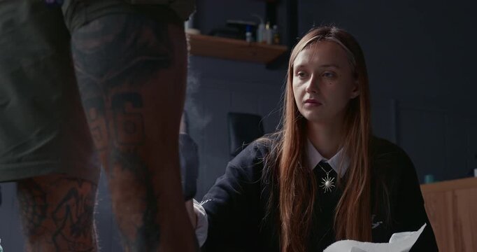 Silhouette of a female tattoo artist preparing a client for a session, standing against a window and a ring light in a studio