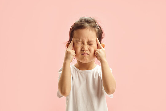 Little Asian girl with tightly closed eyes presses her fingers to her temples, tries to remember something, expresses strong concentration, has forgotten something.trying remember something