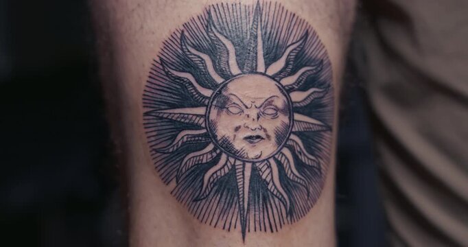  Close-up of a fresh, finished blackwork tattoo of a sun with a face in engraving style on a man's leg