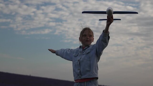 Girl airplane sky, young girl holding toy plane, arms spread wide, imagining flight against cloudy sky.