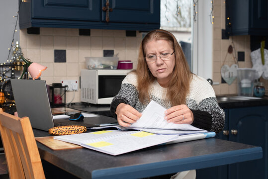 A focused woman reviews documents at a kitchen, surrounded by laptop, notebook, and sticky notes. Cozy home office vibe, suggesting remote work, budgeting, or family organization